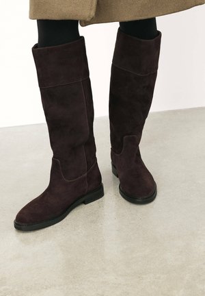 Dunkelbraune Wildleder-Stiefel bis zum Knie mit einer glatten Textur und runder Zehenpartie, die ein einfaches Design und eine flache Gummisohle aufweisen.