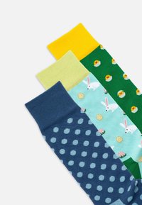 Tre paia di calzini con motivi colorati: polsino giallo, verde con uova, azzurro con coniglietti e blu scuro con pois.
