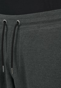Gray jogger pants featuring a textured fabric, elastic waistband with black drawstrings, and metal eyelets. No visible pockets.