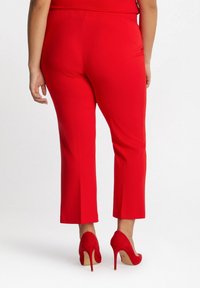 Czerwone dopasowane spodnie o gładkiej teksturze, w skróconej długości i smukłym kroju, w zestawie z dopasowanymi czerwonymi szpilkami.