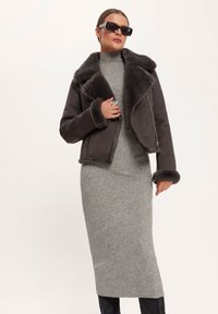 Czarna, ciemnoszara kurtka z baranim futrem z szerokim kołnierzem i mankietami, zestawiona z dopasowaną, jasnoszarą sukienką, zaprezentowana na neutralnym tle.