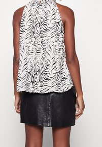 Haut halter à rayures noires et blanches, avec une coupe ample, fabriqué en tissu léger, associé à une jupe en cuir noir ajustée, au toucher lisse.