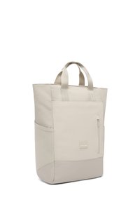 Világos bézs szövetből készült táska, texturált felülettel. Kétszeres fogantyúval és elülső cipzáras zsebbel rendelkezik. Négyzet alakú, egyszínű kiegészítőkkel.