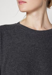 Sudadera de felpa gris carbón con escote redondo y textura sutil, que presenta un ajuste relajado. Sin patrones ni detalles de hardware visibles.