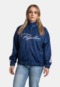 Granatowa kurtka w paski z wysokim kołnierzem, elastycznymi mankietami i paskiem w talii. Białe logo z przodu i kontrastowe białe paski na rękawach.