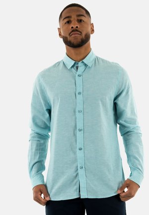 Chemise boutonnée à manches longues de couleur bleu clair, avec un col. Fabriquée dans un tissu texturé, elle présente une patte de boutonnage à l'avant et un ourlet droit.