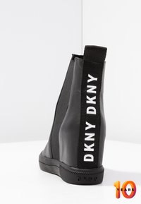 Zwarte enkellaars met een strak ontwerp, elastische zijpanelen, een rubberen zool en een opvallend wit DKNY-logo op de achterkant.