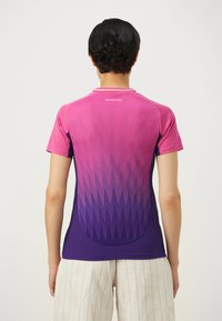 T-shirt de sport à manches courtes dégradé de rose à violet avec un motif géométrique, présentant une encolure ronde et une finition lisse et texturée.