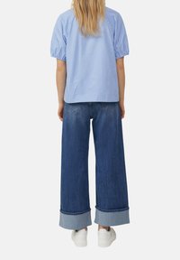 Lichtblauw gestreepte tops met korte mouwen gecombineerd met wijde donker denim jeans. De jeans hebben opgerolde boorden en worden gedragen met witte sneakers.