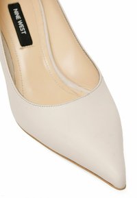 Bež usnjeni čevelj z ostrim nosom, ki se ponaša z gladko teksturo in diskretnimi šivi, označen z "NINE WEST" znotraj.