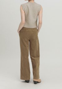 Béžový bezrukávový pletený top s žebrovanými okraji, kombinovaný s hnědými manšestrovými kalhotami s vysokým pasem a širokými nohavicemi. Materiál vypadá jemně a strukturovaně.