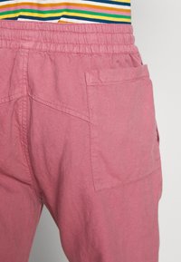 Gros plan sur un pantalon à taille élastique rose avec poche arrière, porté avec un haut rayé coloré.