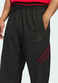 Czarne spodnie sportowe z elastycznym pasem, czerwonymi akcentami i wzorem w trzy paski. Posiadają boczne kieszenie oraz gładką fakturę.