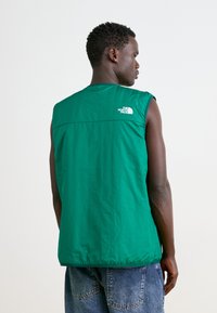 Green sleeveless vest in lightweight material, featuring a subtle quilted texture and branding in white on the upper back.