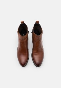 Hnědé kožené kotníkové boty s hladkým povrchem, špičatou špičkou, zipem na jedné straně a poutkem na patě.