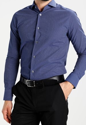 Blau gemustertes Hemd mit Knöpfen, das einen Kentkragen, lange Ärmel und eine schlanke Passform aufweist, kombiniert mit schwarzen Hosen und einem schwarzen Gürtel.