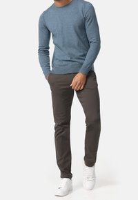 Ljusblå stickad tröja med ribbad halsringning och muddar, i kombination med mörkgrå slim fit-byxor och vita sneakers. Minimalistisk design, inga mönster.