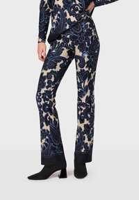 Blommönstrade byxor i marinblå och beige tyg, med en slät yta och skräddarsydd passform. Komplementeras av enfärgade svarta ankelstövlar.