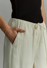 Løse, cremefarvede bukser med en tekstureret overflade, elastisk talje og synlig sidelomme. Justerbar snøre detaljer.