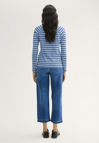 Modrý pruhovaný top s dlouhým rukávem v kombinaci s modrými džínami s širokými nohavicemi. Boty jsou černé s texturovaným povrchem. Zaměření na ležérní oblečení.