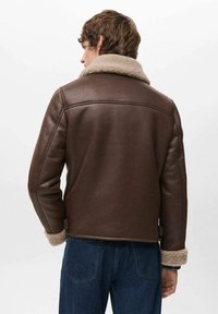 Giubbotto di pelle marrone con colletto in pelliccia. Presenta una texture liscia e un design aderente. Visto da dietro, abbinato a jeans blu.