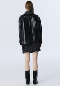 Giacca in finta pelle nera con colletto borchiato, maniche lunghe e vestibilità rilassata. Abbinata a una gonna nera plissettata e stivali neri fino al ginocchio.