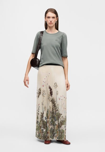 Φορώντας ελαφρώς πράσινο ριμπ τοπ με κοντά φουσκωτά μανίκια, συνδυασμένο με πλισέ φούστα με floral μοτίβο σε παστέλ αποχρώσεις και τσάντα που ταιριάζει.