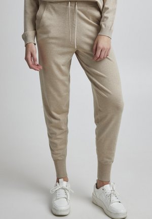 Helle beige Jogginghosen aus weichem Material, mit elastischem Bund und Kordelzug, seitlichen Taschen und schmal zulaufendem Bein. Kombiniert mit weißen Sneakers.