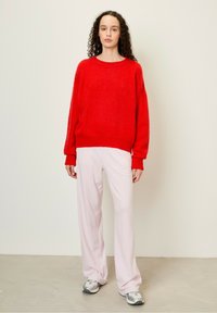 Raudonas, pūkuotas megztinis su apvaliu kaklu, derinamas su šviesiai rožiniais, laisvai krentančiais kelnėmis ir pilkais sportiniais batais. Lygi tekstūra, kasdienis stilius.