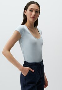 Jasnoniebieski gładki bodysuit z szerokim okrągłym dekoltem, w zestawieniu z granatowymi spodniami na sznurek. Gładka faktura, dopasowany krój, krótkie rękawy.