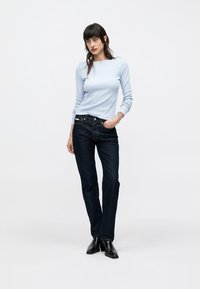 Jasnoniebieska bluzka z długim rękawem o okrągłym dekolcie, zestawiona z ciemnoniebieskimi dżinsami i czarnymi botkami za kostkę. Luźny fason, gładka faktura.