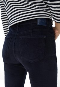 Marineblauwe corduroy broek met achterzakken, gedragen met een zwart-witte horizontaal gestreepte lange mouwtop.