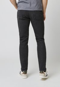 Vaqueros de mezclilla negros con un corte ajustado, que presentan bolsillos traseros y una textura ligeramente desgastada. Combinados con zapatillas blancas, mostrando un estilo casual.