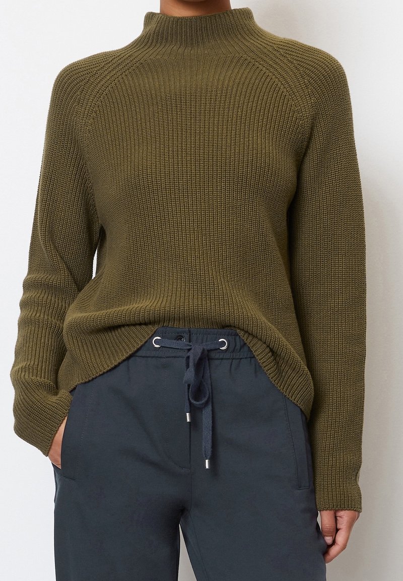 Olivgrüner, gerippter Strickpullover mit hohem Kragen, der Raglanärmel und einen leicht längeren hinteren Saum hat.