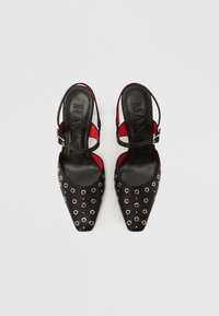 Fekete slingback cipőkhegyes orral, ezüst fémkarikákkal és piros párnázott talpbéléssel. Csiszolt bőrből készült, elegáns kialakítással.