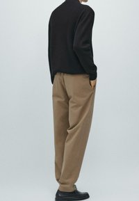 Černý pletený svetr v kombinaci s béžovými volnými kalhotami a černými botami. Tkanina působí měkce a outfit má minimalistický design.