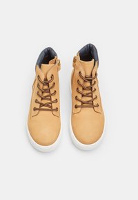 Zapatillas altas de cuero marrón con suelas blancas, cuello acolchado negro, cordones marrones y cremallera lateral. Textura suave con detalles de costura mínimos.