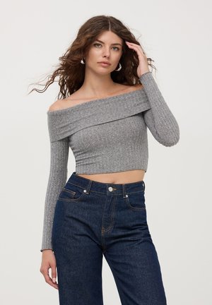 Cropped top grigio a costine con spalle scoperte e maniche lunghe, abbinato a jeans scuri in denim a vita alta con tasche tradizionali e chiusura con bottone.