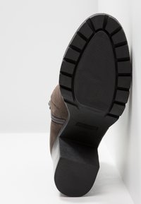 Bottine en suède marron avec une semelle en caoutchouc noir épaisse, dotée d'une fermeture éclair diagonale et d'un motif texturé pour l'adhérence.