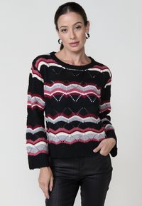 Pull en tricot avec une base noire, présentant des motifs en zigzag rouges, roses et gris. Coupe ample, encolure ronde et manches longues.