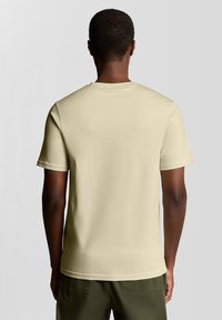 Gaiši bēša īsroku t-krekls ar apaļu apkakli, izgatavots no mīksta auduma ar bezšuvju plecu dizainu un minimālistisku stilu.