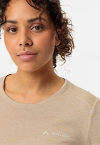 Beige teksturert t-skjorte med rund hals, med en subtil VAUDE-logo på venstre side. Stoffet ser mykt og lett ut.