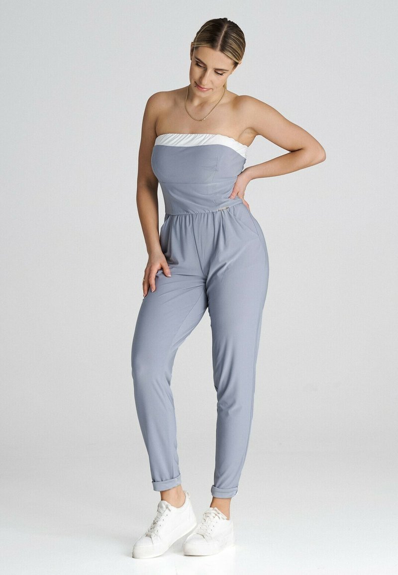 Jumpsuit bez ramiączek w jasnoszarym kolorze z białą górną częścią, elastycznym paskiem w talii i zwężanymi nogawkami. Noszony z białymi sneakersami, minimalne detale.