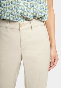 Béžové bavlněné kalhoty s hladkou texturou, s knoflíkovým zapínáním, předními kapsami a standardním střihem. Doplněné květinově vzorovanou blůzou.