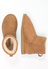 Bottines en suède beige avec doublure douce, bout rond et semelle en caoutchouc plate. Présentent une couture et une petite sangle à l'arrière.