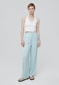 Witte halter crop top en lichtblauwe wijde broek van gladde stof, met een elastische tailleband, gecombineerd met zwarte flip-flops.