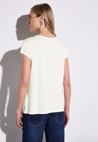 Cremefarvet kortærmet T-shirt med en afslappet pasform, der har en rund halsudskæring og sideslids, parret med mørkeblå jeans.