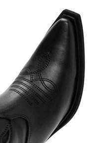 Bota de vaquero de cuero negra con punta afilada, detalles de costura en relieve y una textura suave; sin herrajes o acentos visibles.