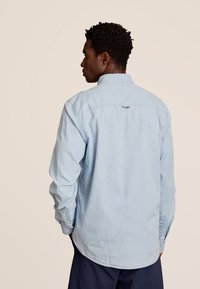 Lichtblauw overhemdd met lange mouwen, gemaakt van zachte stof, met een afgeronde zoom en een klein logo-detail op de bovenrug.