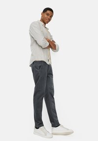 Lichtgrijs gestreept overhemd over een crème top; donkergrijze corduroy broek en witte sneakers. De fit is relaxed.
